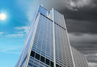 Staring up the side of a tall glass office building with blue sky on one side of it and dark clouds on the other.