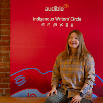 A woman sits on a bench in front of a red sign that has Audible's logo and says Indigenous Writers' Circle.