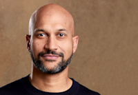 Close headshot of Keegan-Michael Key with a shaved head, mustache and beard and wearing a black shirt against a beige background.