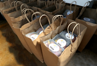 Brown paper bags with handles sit set up in a row and filled full of meals packaged in plastic containers with NWK logos on them.
