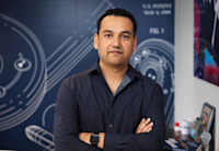 Shailesh looks sternly at the camera with his arms folded. Behind him is a blueprint style wallpaper.