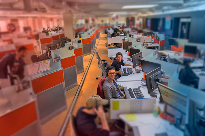 Audible Customer Care employees seated at their desks. Several rows of cubicles extend from the front of the back to the room.