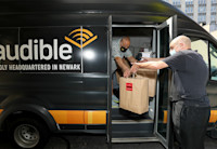 A man in a delivery van, with an Audible logo on the side, hands two large paper bags full of Newark Working Kitchen meals out the van door to a man standing on the street.
