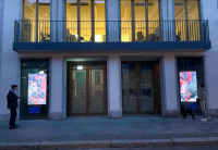 a building with glass doors, a balcony, and two multimedia screens with artwork