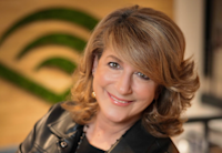 Anne Erni smiles at the camera while leaning slightly back with her arms folded. She's wearing a black leather jacket, and the Audible logo is out of focus in the background.