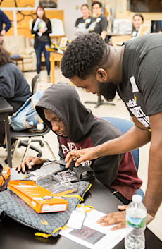An Audible employee assists a high school student, seated at a table, with setting up his tablet to listen to Audible as part of Project Listen Up.