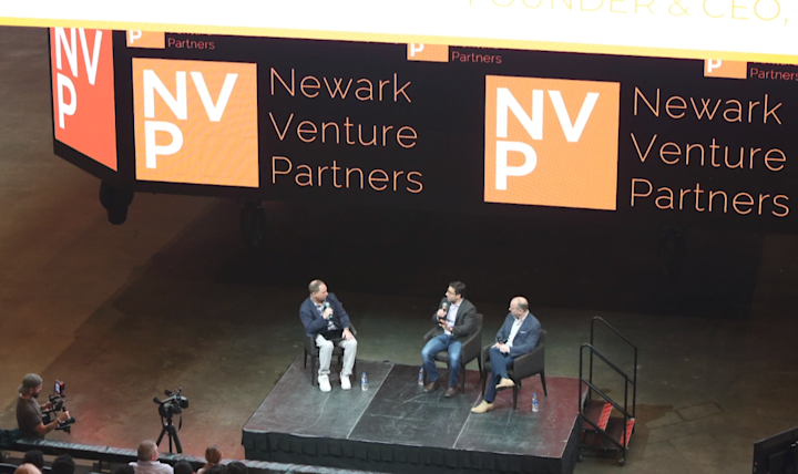 Three people sit on stage for a panel discussion under a large Newark Venture Partners sign.