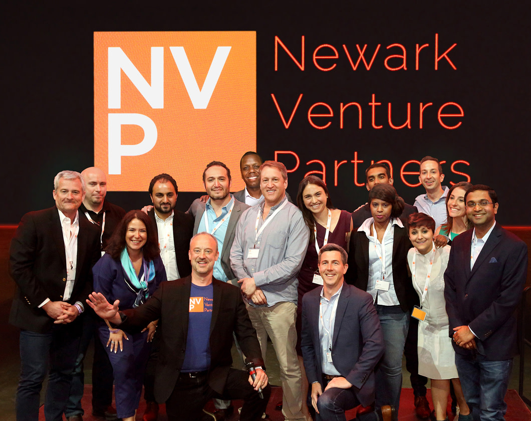 A group of tech start up founders standing in front of the Newark Venture Partners logo.