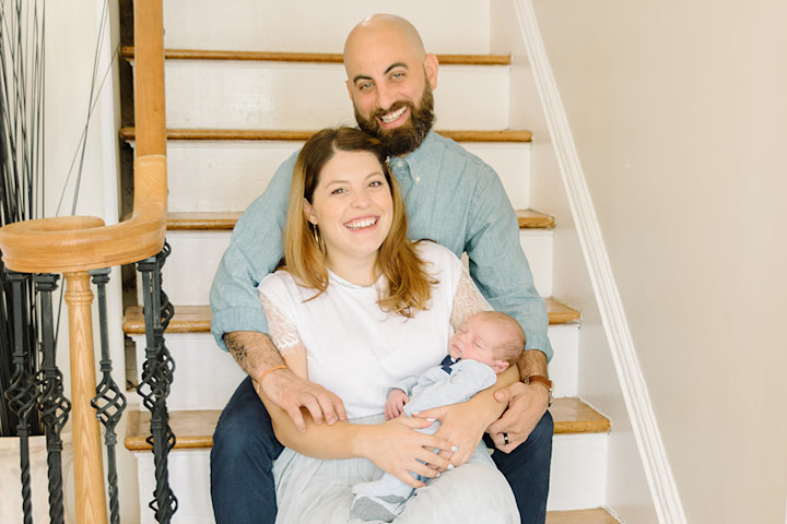 A couple with their new baby sit on the staircase of their home in Newark.