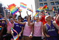 People crowded together to watch the NYC Pride March. They're wearing pink and purple #BeEpic shirts and waving rainbow-colored Pride flags.