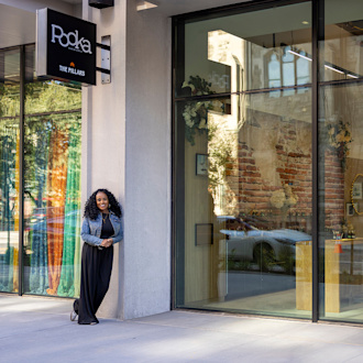 A woman stands outside the glass windows of a store with the sign with the store name "Pooka" above her head.