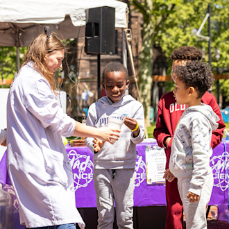 A woman shows a science experiment to three small children.