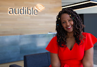 A woman in a red dress sitting in front of the Audible logo.