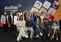 A group of actors and Audible employees gathers together in front of a backdrop with audiobook cover art and the Audible Brazil logo.