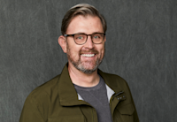 A headshot of James Finn. James is wearing glasses, a gray shirt, and a green jacket. He's smiling.