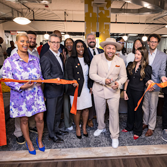 A crowd of people stand at a ribbon cutting ceremony, the guy at the center having just cut it to mark the space's opening.