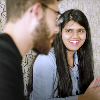 Two people sit in a booth in Audible's Newark offices talking with one another. The woman faces toward us, smiling. The man is front of frame and slightly blurry as seen in profile.