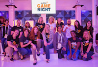 A large group of women wearing t-shirts with Audible's logo pose together before an Audible Game Night sign.