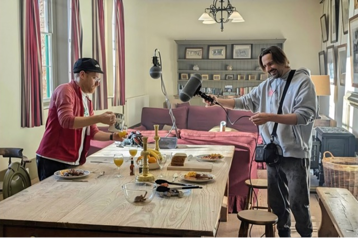 A photo of two sound designers capturing audio of dinner plates and silverware moving around a table.
