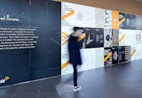 An employee dressed in all black is walking past a wall in our lobby that outlines all of our people principles and our new design featuring lines in various patterns for each of our principles.