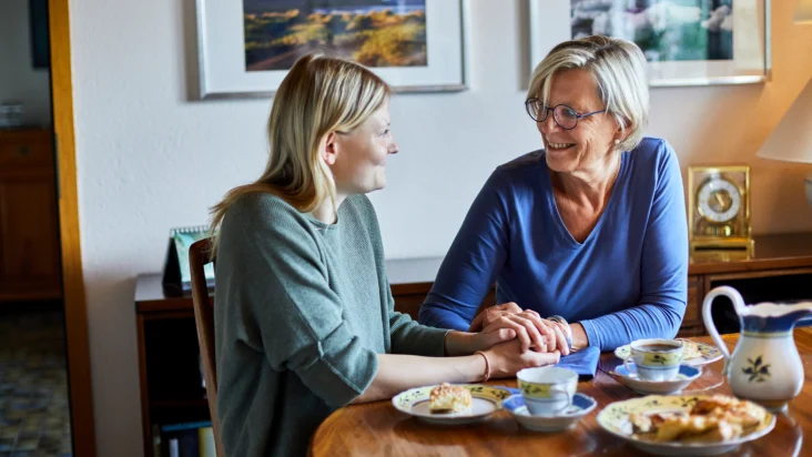 A mother and daughter clasp hands while smiling at a breakfast table