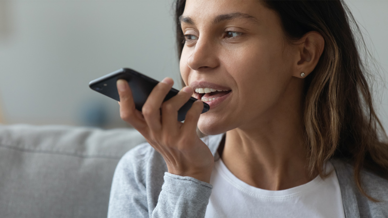 Photograph of a person holding and speaking into a smartphone, meant to symbolize voice technology