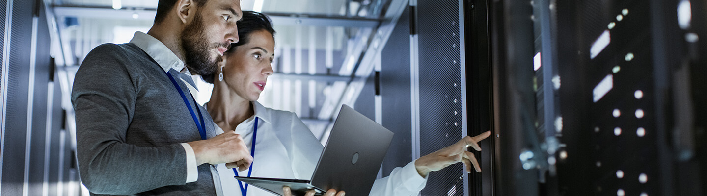 A man and woman looking at a computer server inside of a server room