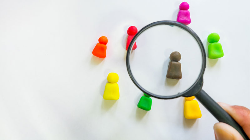 magnifying glass looking at colorful clay figures representing people to hire