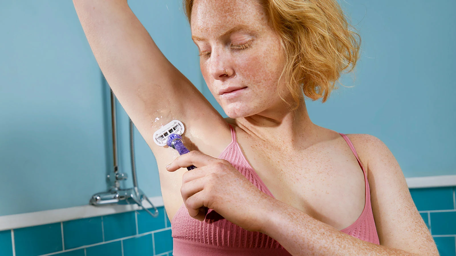 Kvinna som rakar armhålan med en rakhyvel i ett badrum