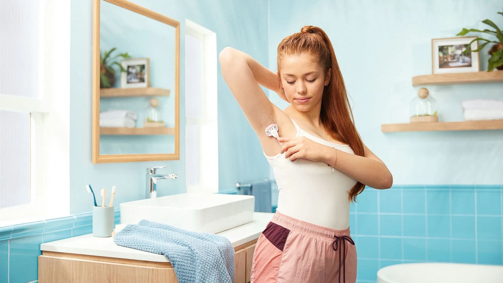 Ung kvinna i vit linne rakar armhålorna i badrummet