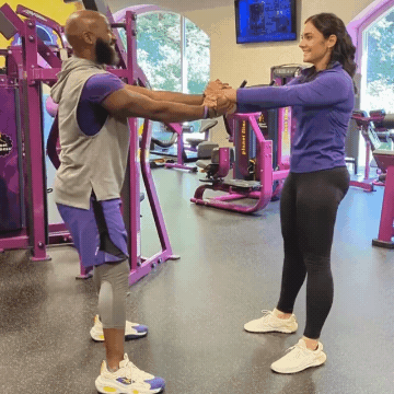 Man and woman working out in Planet Fitness gym doing squats while grasping hands