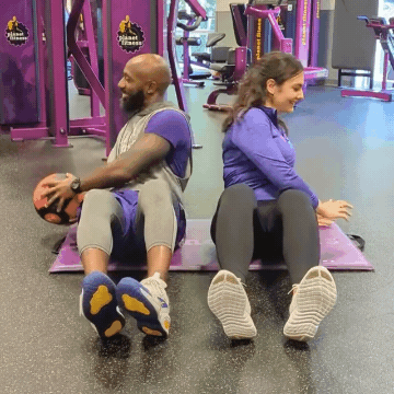 Man and woman working out in Planet Fitness gym doing medicine ball Russian twists