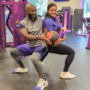 Man and woman working out in Planet Fitness gym doing medicine ball squats with a pass