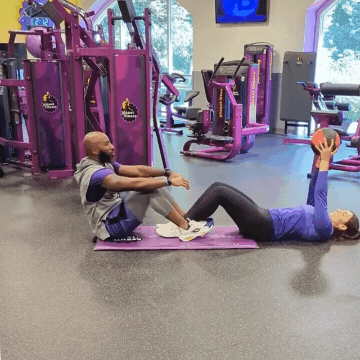 Man and woman working out in Planet Fitness gym doing medicine ball sit-up passes