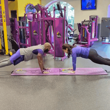 Man and woman working out in Planet Fitness gym doing plank high fives