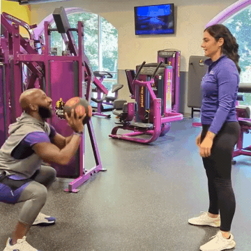 Man and woman working out in Planet Fitness gym doing medicine ball squat tosses