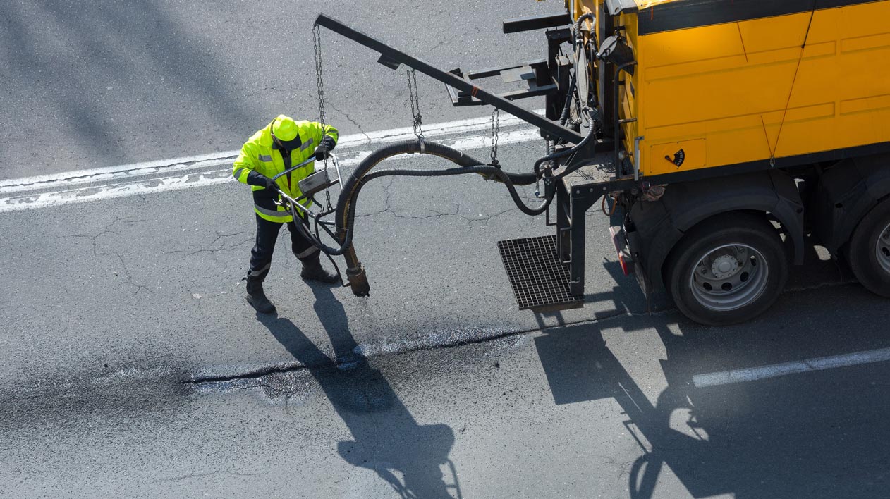A construction worker in a high-visibility jacket uses equipment to repair a road.