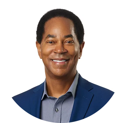 A man in a blue suite jacket and light blue button-up shirt smiles.