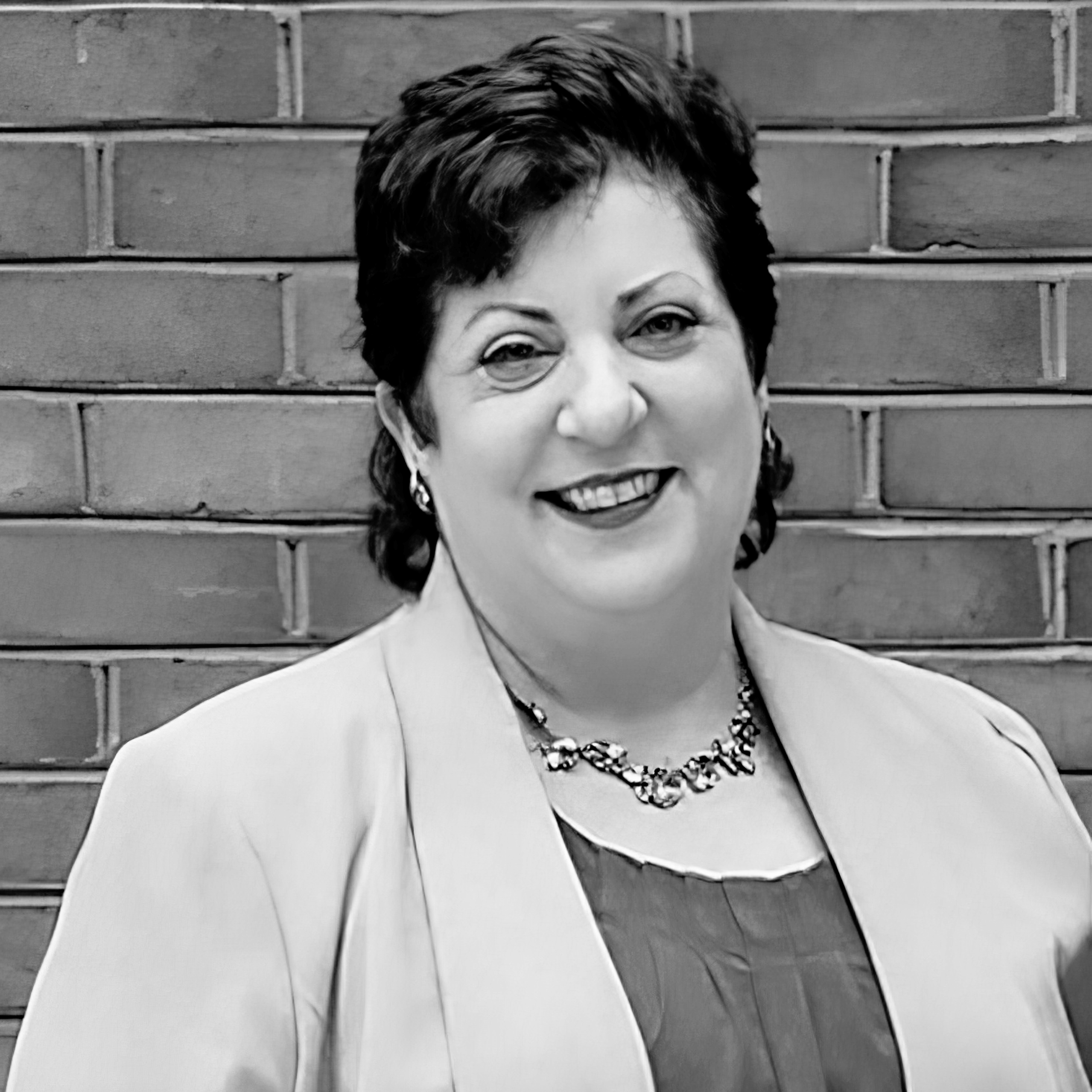 Foto del rostro de Amy Menrad, con una bluza azul brillante y una chaqueta amarilla, al aire libre.