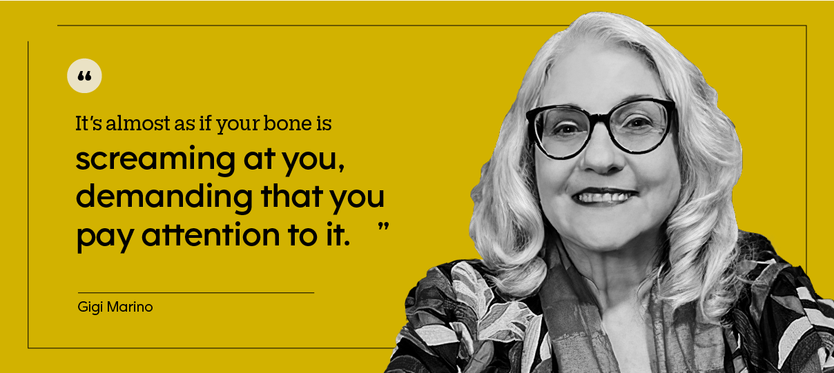 Portrait of Gigi Marino, who is wearing a colorful jacket and sitting in front of a bookcase.
