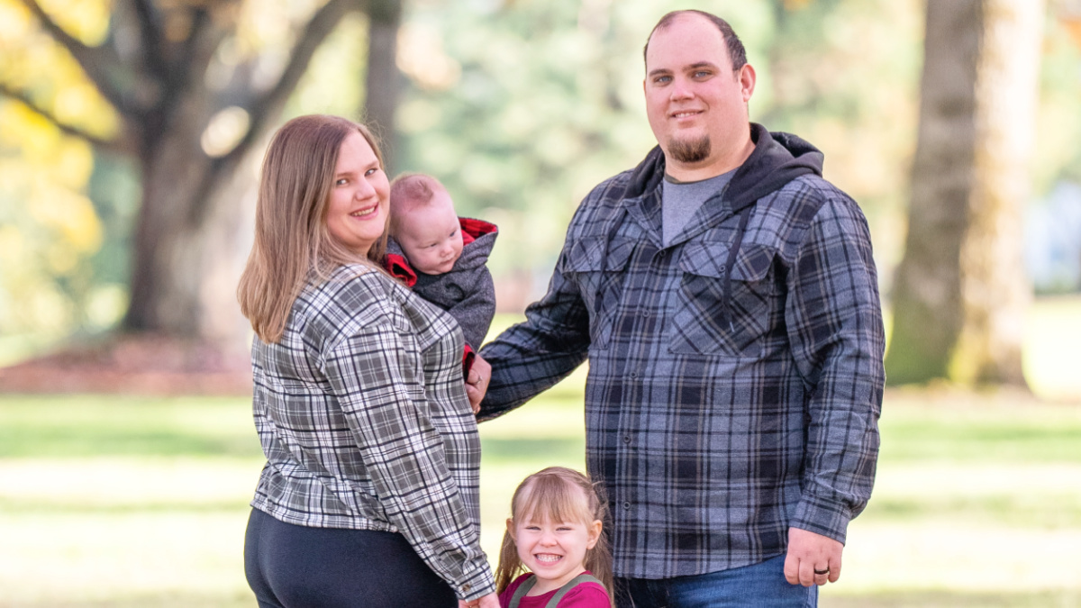 Emily Pierzina is pictured in a family portrait in a park-like setting with her husband, toddler daughter, and infant son.