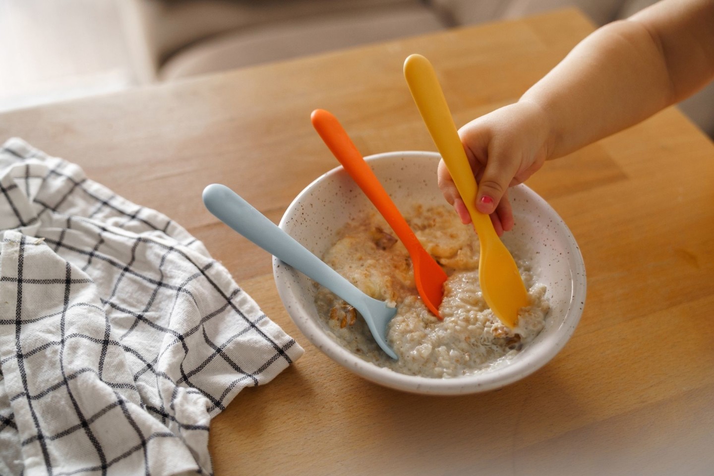 Baby hand reaching for a spoon in a bowl of oatmeal