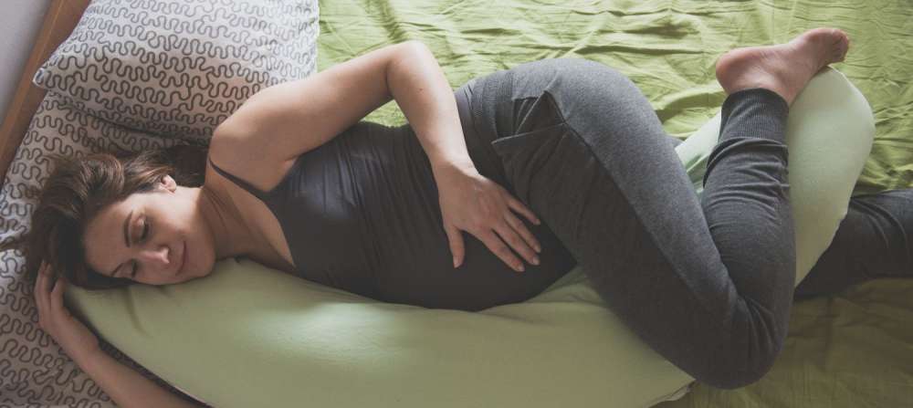A pregnant woman laying on her side using a C-shaped pregnancy pillow.