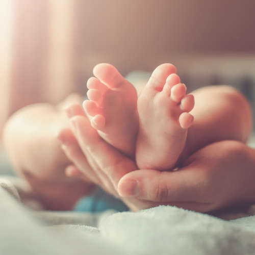 Adult hands holding baby feet in crib