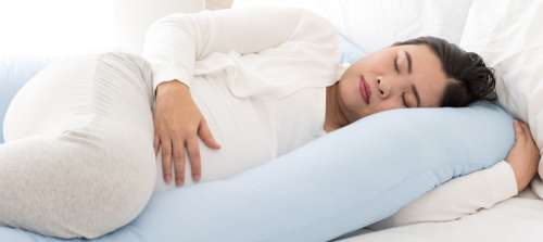 A pregnant woman sleeping with a pregnancy pillow. 