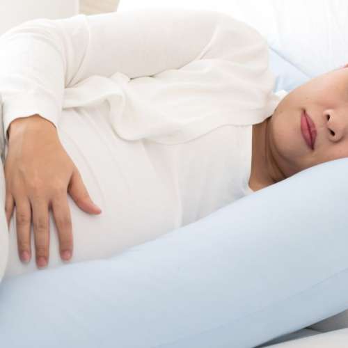 A pregnant woman sleeping with a pregnancy pillow. 