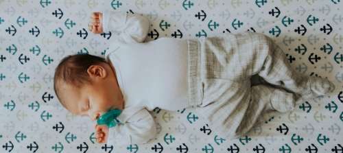 A baby sleeping on their back with a pacifier. 