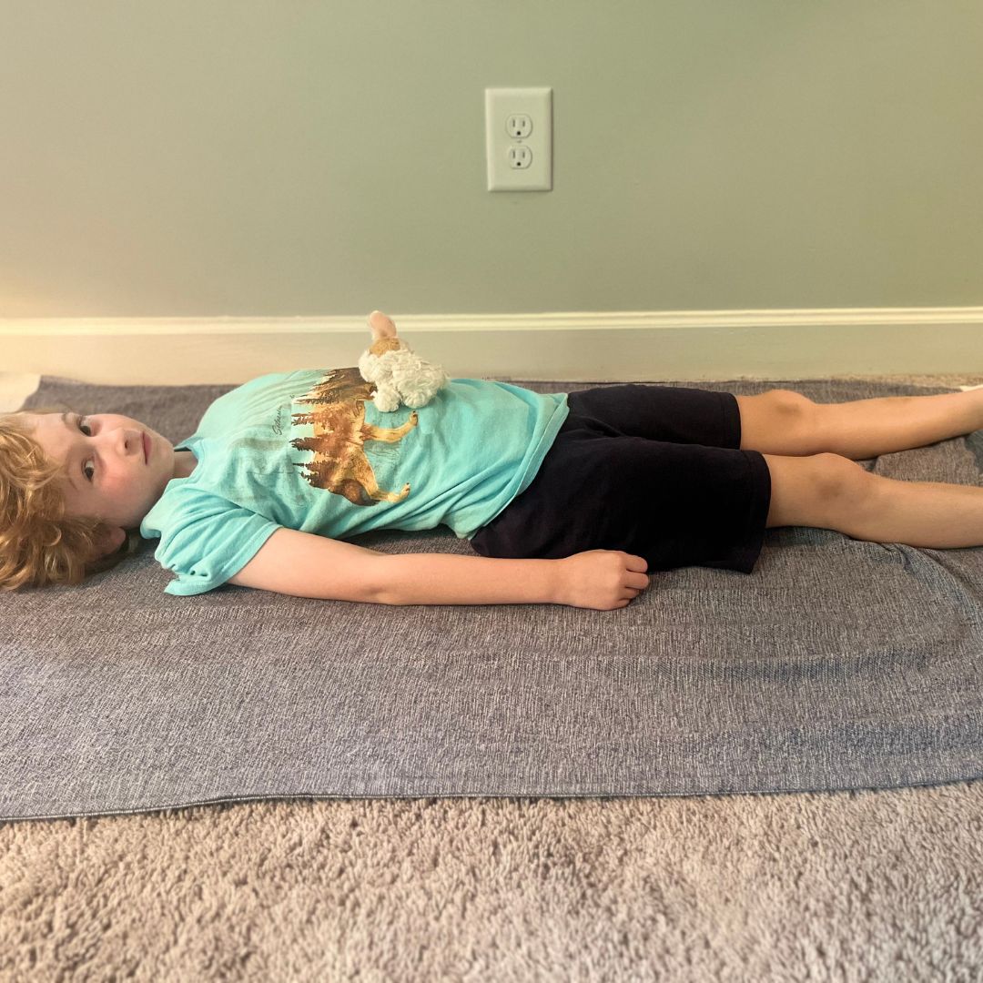 A child doing a relaxation yoga pose with a stuffed animal on the belly. 