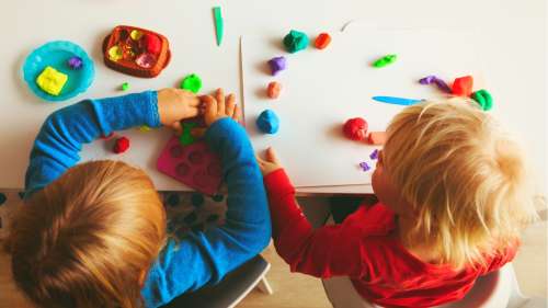 two kids playing on table with play doh