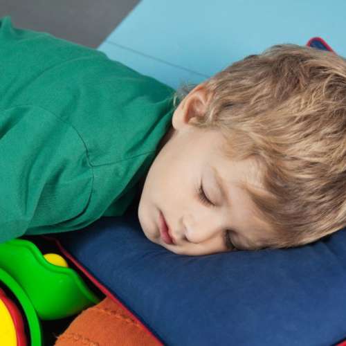 A kindergartener boy is napping on a nap mat.